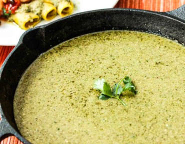 A black cast-iron skillet filled with pumpkin seed (Pipián) sauce with a sprig of cilantro in the middle.