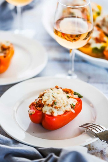 A single turkey and rice stuffed bell pepper sitting on a white plate next to a glass of wine.