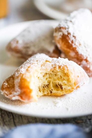 A close-up view of a half-eaten beignet covered in powdered sugar sitting on a white dessert plate.