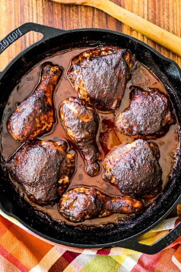An overhead view of baked chicken mole pieces in a large black cast-iron skillet sitting next to a large wooden spoon.