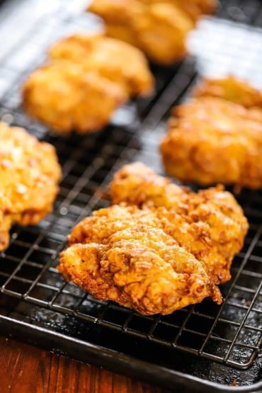 A close-up view of a crispy deep-fried chicken cutlet sitting on a baking rack over a baking sheet.