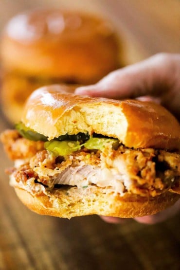 A person holding a crispy fried chicken sandwich that has a bite taken out of it.