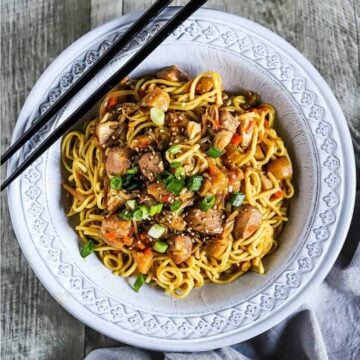 An overhead view of a grey bowl filled with slow-cooker chicken chow mein flanked by two black chopsticks.