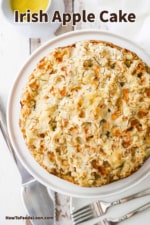 An overhead view of an untouched Irish apple cake with a pie slicer and a couple of forks nearby.