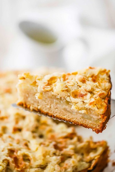 A slice of Irish apple cake being raised up the entire cake on a silver pie slicer.