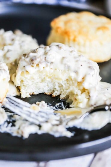 A homemade Southern biscuit covered in sausage gravy with a bite take out of it.