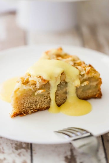 A slice of Irish apple cake topped with vanilla custard sitting on a white dessert plate.