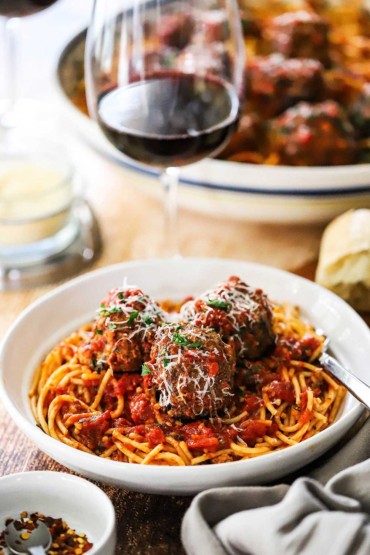 A close-up view of a white bowl filled with a serving of spaghetti and meatballs with parmesan cheese shredded over the top.