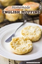 An un-toasted English muffin that has been split open and placed on a white plate next to a butter knife.