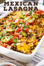 A close-up view of a Mexican lasagna in a white 9 by 13 baking dish topped with chopped tomatoes and slices of jalapeños.