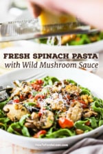 A person grating a block of Parmesan cheese over a pasta bowl filled with spinach linguine with sautéed wild mushrooms and tomatoes.