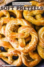 A close-up view of freshly baked soft pretzels sprinkled with coarse salt stacked on top of each other on a black circular platter.