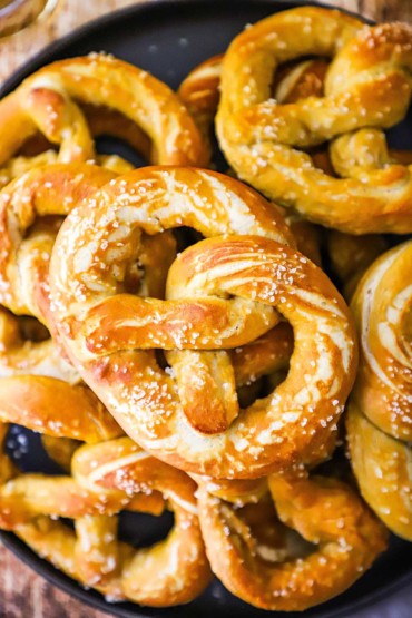 A close-up view of freshly baked soft pretzels sprinkled with coarse salt stacked on top of each other on a black circular platter.