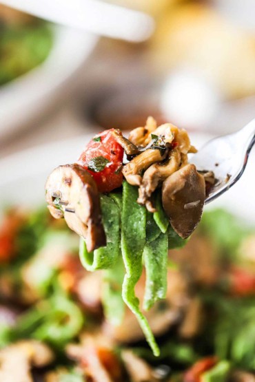 A fork holding up a helping of spinach pasta with wild mushroom sauce.