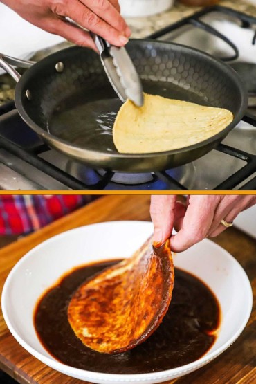 A person using a pair of metal tongs to turn a corn tortilla in a small skillet with hot oil and then coating that same tortilla in a bowl of enchilada sauce.
