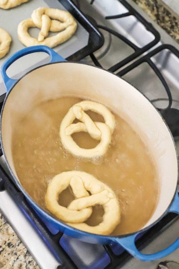 Two uncooked pretzels in an oval Dutch oven filled with boiling water on a stovetop.
