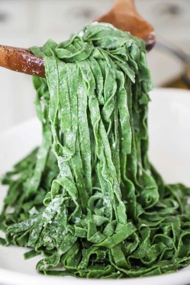 A large wooden spoons lifting up cooked fresh spinach pasta from a bowl.