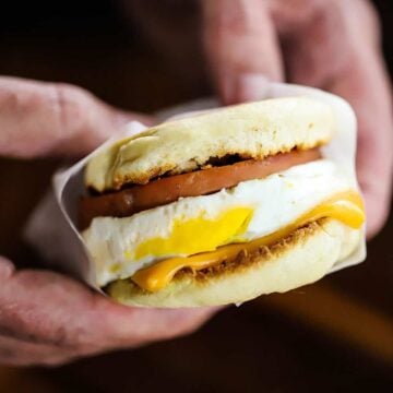 A person holding an egg mcmuffin copycat that has been wrapped in white wax paper.