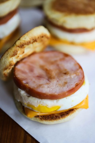 An overhead view of an Egg McMuffin copycat sandwich that is sitting on a wax pepper with the top toasted English muffin resting off to the side.