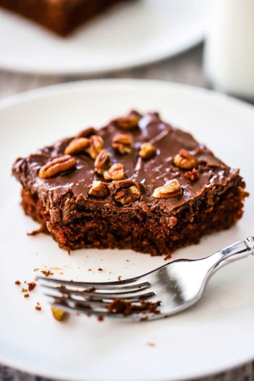 A close-up view of a square piece of Texas sheet cake with a bite of it missing and a fork sitting nearby.