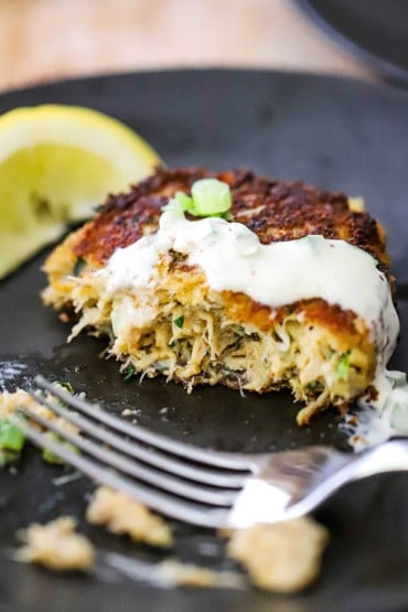 A close-up view of a crab cake topped with a jalapeño remoulade and has been half eaten.