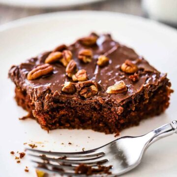 A close-up view of a square piece of Texas sheet cake with a bite of it missing and a fork sitting nearby.