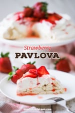 A slice of strawberry pavlova on a white dessert plate with the pavlova sitting on a cake stand in the background.