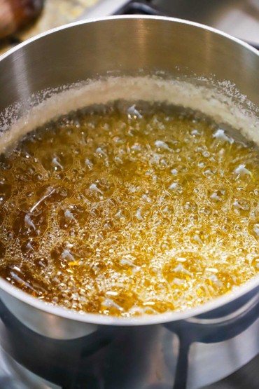 A stainless steel saucepan filled with sugar water that is bubbling intensely and is an amber color.