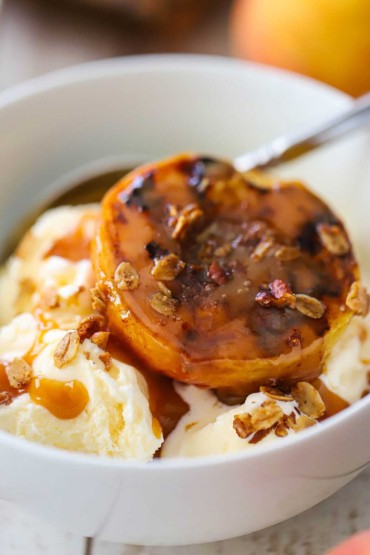 A close-up view a grilled peaches and caramel sitting on vanilla ice cream with homemade granola sprinkled on top.
