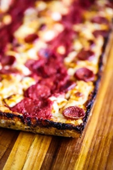 An close-up view of the end corner of a pan pizza with caramelized edges and crispy pepperoni on top.