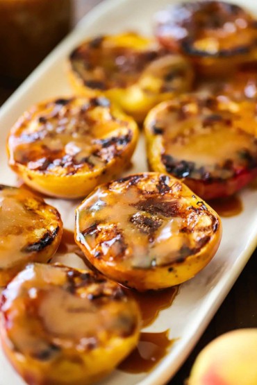 A close-up view of grilled peaches with homemade caramel sauce all on a white rectangular platter.