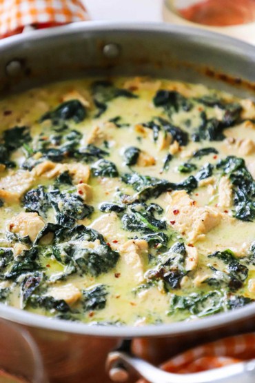 A close-up view of a large stainless steel skillet filled with creamy chicken florentine. 