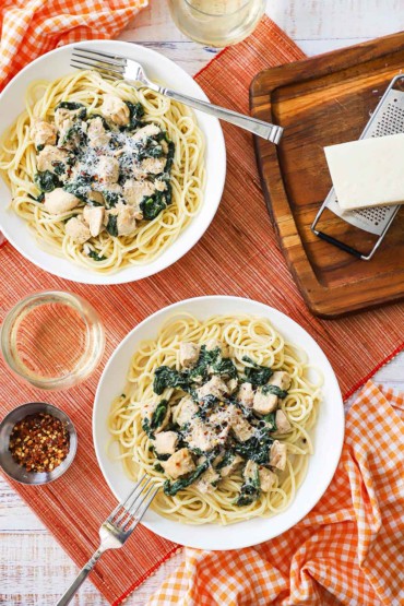 An overhead view of two pasta bowls filled with creamy chicken florentine both sitting on a bed of cooked pasta. 