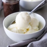 A close-up view of a white dessert bowl filled with several scoops of homemade vanilla ice cream.
