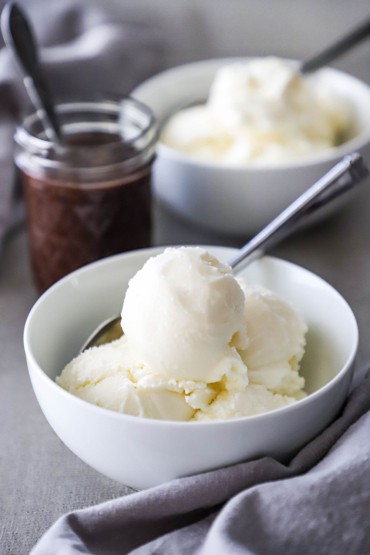 A close-up view of a white dessert bowl filled with several scoops of homemade vanilla ice cream.