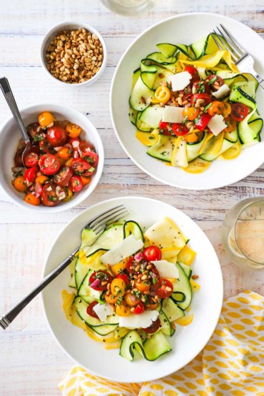 An overhead view of two bowls filled with a zucchini and yellow squash salad with tomato relish sitting next to another bowl filled with the tomato relish.
