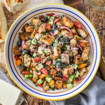 An overhead view of a large pasta bowl filled with panzanella and flanked by a block of Parmesan cheese and a torn loaf of bread.