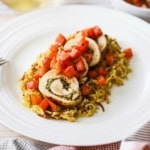 A close-up view of plate filled with sliced pesto-stuffed chicken with tomato relish all on a bed of rice pilaf.