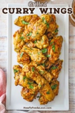 An overhead view of a pile of grilled curry chicken wings topped with chopped cilantro on a white rectangular platter.