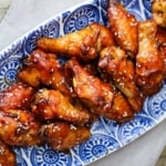 An overhead view an oval blue platter filled with a pile of teriyaki chicken wings.