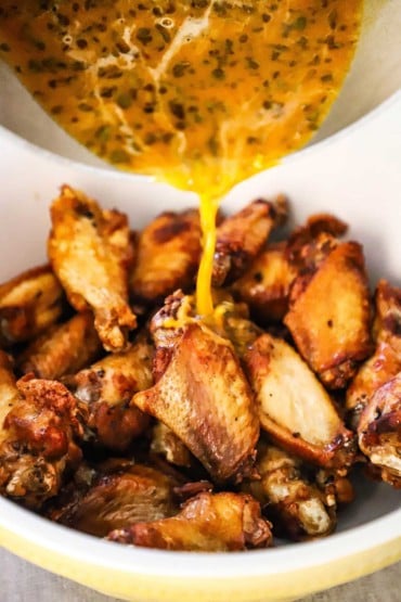 Italian-style wing sauce being poured over a bowl of chicken wings that have been deep-fried and are golden in color.