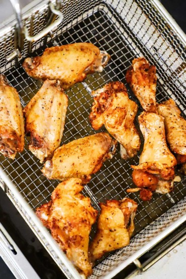An overhead view of a deep fryer basket holding freshly fried chicken wings.