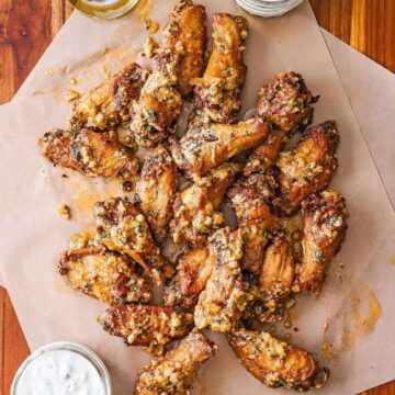An overhead view of a serving of garlic Parmesan wings on two pieces of brown paper with a small jar of blue cheese dressing nearby.