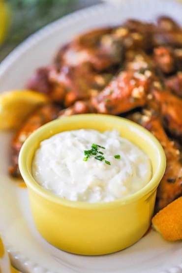 A straight-on view of a small yellow bowl that is filled with a gorgonzola dipping sauce and is sitting on a platter next to a pile of cooked wings.