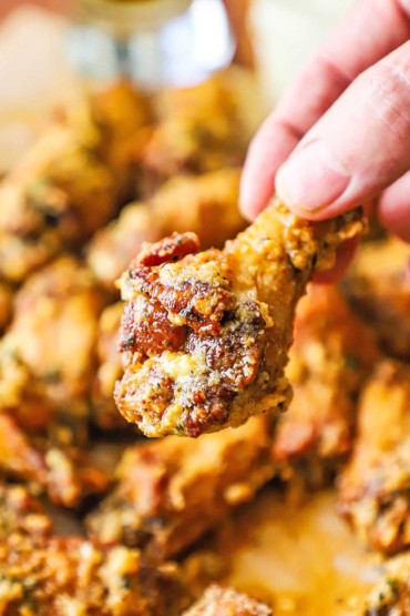 A person holding a garlic Parmesan chicken wing over a pile of the same wings.