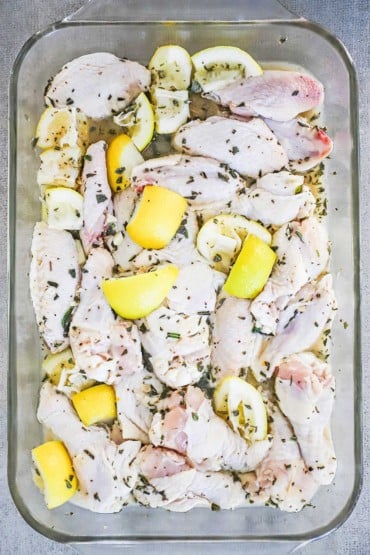 An overhead view of 2 pounds of uncooked chicken wings in a glass casserole dish soaking in a lemon and herb marinade.