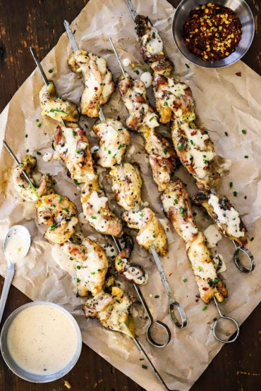 An overhead view of grilled chicken skewers with Alabama sauce on a piece of crumpled brown wax paper.