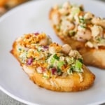 A close-up view of two pieces of toasted crostini that are both topped with an albacore tuna and white bean salad that has toasted bread crumbs on top .