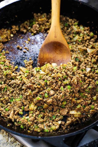 A straight-on view of a large cast-iron skillet partially filled with Cajun dirty rice with a wooden spoon inserted into the middle.