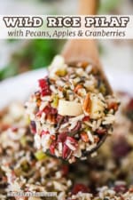 A large wooden spoon holding up a heaping helping of wild rice with pecans and cranberries stuffing.